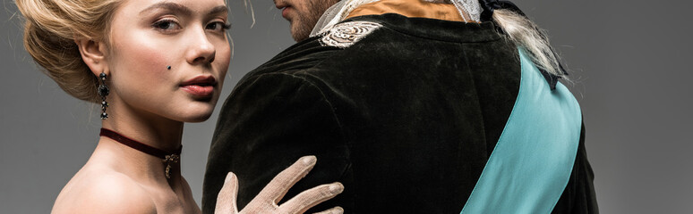 panoramic shot of beautiful victorian woman hugging gentleman in wig isolated on grey