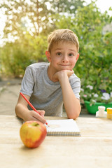 Fototapeta premium Cute boy draws with pencils still life. Open air. Garden in the background. Creative concept.
