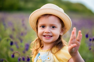 Cute smiling baby girl in beige hat outdoors in green field. Child portrait