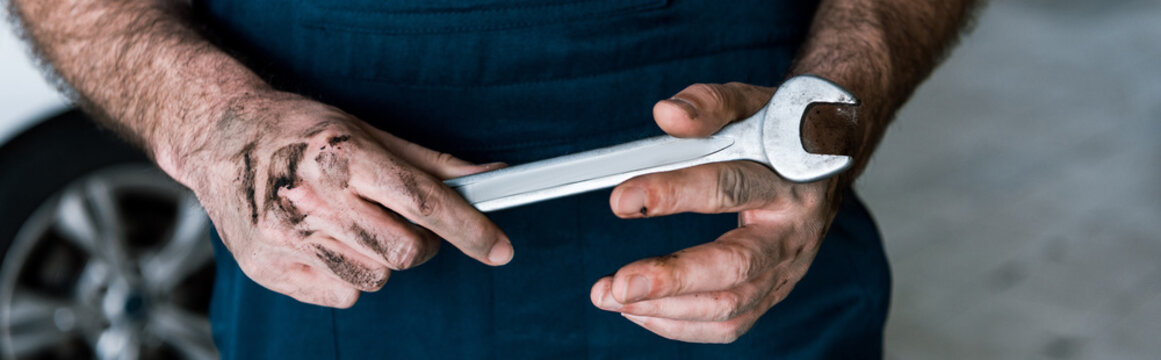 panoramic shot auto mechanic with mud on hands holding hand wrench in car repair station