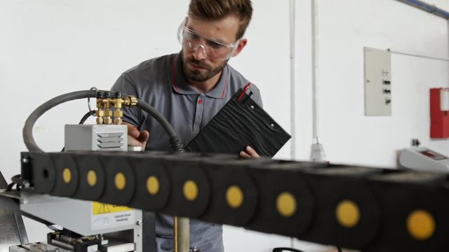 Young engineer setup plasma cutter for work in metalwork workshop.