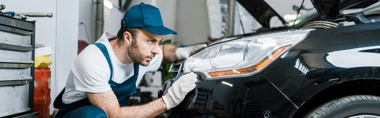 panoramic shot of handsome bearded car mechanic looking at tail light in black car