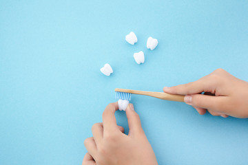 child's hand with toothbrush and white platic tooth on blue background