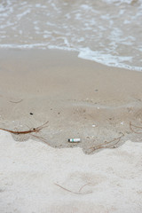 A white cigarette butt left trashed on the beach that will cause environment problem.