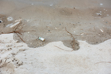 A white cigarette butt left trashed on the beach that will cause environment problem.