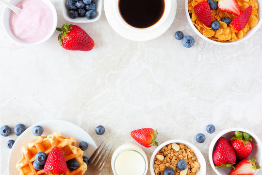 Breakfast food double border. Fruits, cereal, waffles, yogurt, coffee and milk. Top view over a bright stone background with copy space.