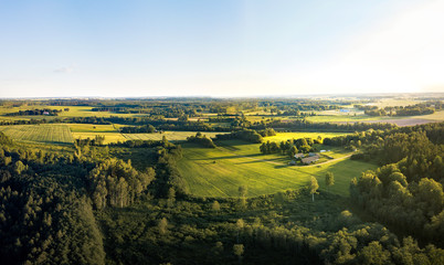 Aerial view over rural landscape in a warm summer sunset tones. Agriculture land mixing with forest and meadows. Green crop fields along the curved river. Trees creating long shadows. 