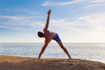 Fototapeta na wymiar Young athletic man practicing yoga asana pose near the sea beach