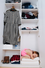 Portrait of little girl in new pink overalls playing inside of open wardrobe