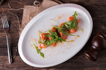 Fresh sliced salmon fillet with arugula on white plate and rustic table