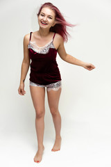 Concept portrait of a full-length pretty sexy girl with purple hair in beautiful red lingerie on a white background. She smiles, happy with life, happy. Hair flying, front view. Made in a studio.