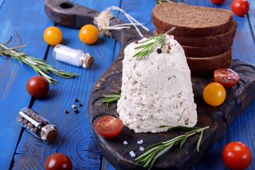 Homemade cheese with greenery and spices on the board on the blue wooden table