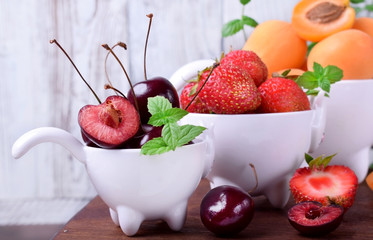 Cherries, strawberries and apricots in little white cups on the wooden table
