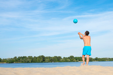 A man playing beach volleyball on hot sand on a sunny day.  Back view.  Sports  lifestyle.