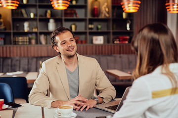 Two multicultural smiling colleagues dressed smart casual sitting in restaurant and discussing about project.