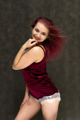 Fototapeta na wymiar Concept portrait of a knee-high pretty sexy girl with purple hair in beautiful red lingerie on a gray background. She smiles, happy with life, happy. Hair flying, front view. Made in a studio.