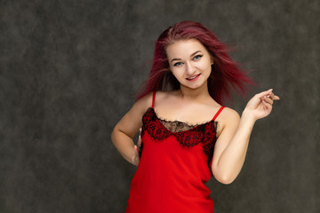 Fototapeta premium Concept portrait of a pretty sexy girl with purple hair in beautiful red lingerie on a white background. She smiles, happy with life, happy. Hair flying, front view. Made in a studio.