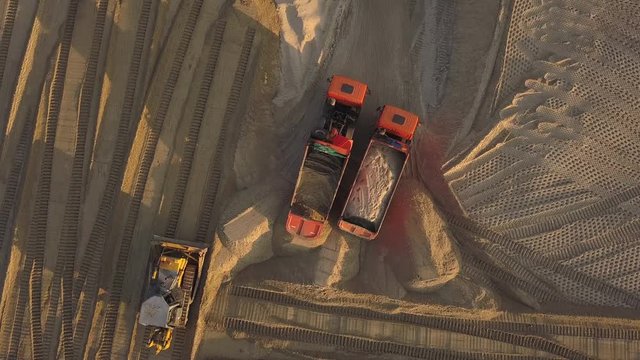 Construction site on the road construction site. Dump trucks with sand unload cargo at the construction site on a summer evening at sunset. Aerial view