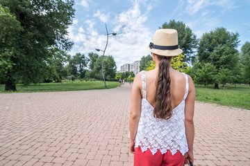 Beautiful young positive and independent French hipster girl walking in the park in the city with hat and sunglasses in retro or vintage fashion clothes view from back on long hair