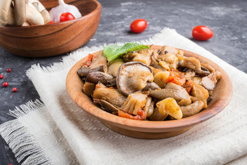 Fried oyster mushrooms with tomatoes in wooden plate on black concrete background. side view.