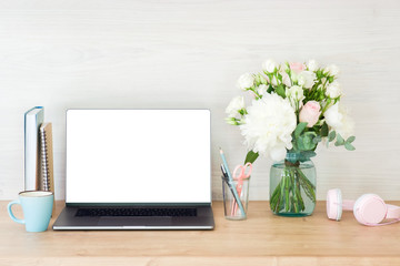 Laptop computer with white blank screen, coffee cup, flowers bouquet and accessories on work table. Business and education concept. Feminine home office workspace