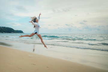 woman jumping happy in the beach with a blue sky and sea in the background