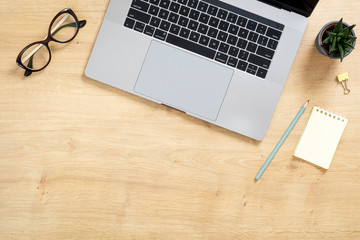 Modern wooden office desk table with laptop computer, paper notepad, succulent plant, glasses. Top view with copy space, flat lay. Feminine workspace concept.