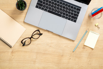 Modern wooden office desk table with laptop computer, paper notepad, succulent plant, glasses. Top view with copy space, flat lay. Feminine workspace concept.