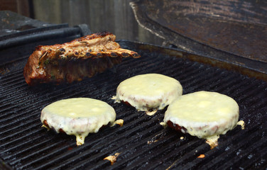 Three cheeseburgers and a rack of lamb on a grill
