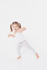 Fototapeta na wymiar a little girl indulges in a white background: dancing, shy, shows her thumb