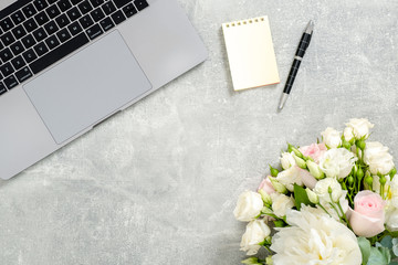 Woman office desk table with laptop computer, flowers, yellow notepad, stationery on concrete stone background. Flat lay, top view feminine workspace