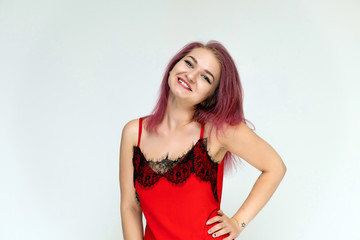 Fototapeta premium Concept portrait of a pretty sexy girl with purple hair in beautiful red lingerie on a white background. She smiles, happy with life, happy. Hair flying, front view. Made in a studio.