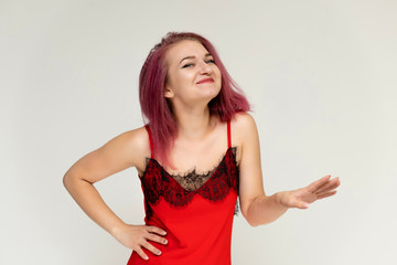 Concept portrait of a pretty sexy girl with purple hair in beautiful red lingerie on a white background. She smiles, happy with life, happy. Hair flying, front view. Made in a studio.