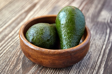 Avocados in a bowl on wooden background. Whole green fresh tropical fruits on brown table