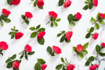 Floral pattern made of red roses flowers, green leaves, branches on white marble background. Flat lay, top view. Mother's day background. Flowers pattern, floral composition.