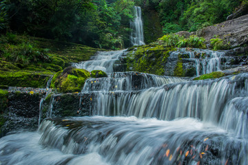 Fototapeta premium Una gran cascada al fondo y el agua corriendo en larga exposicion entre la naturaleza