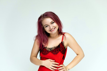 Concept portrait of a pretty sexy girl with purple hair in beautiful red lingerie on a white background. She smiles, happy with life, happy. Hair flying, front view. Made in a studio.