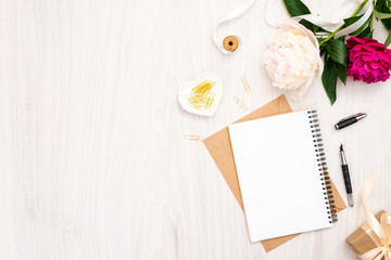 Flat lay home office desk. Female workspace with paper notebook, bouquet of pion flowers, golden accessories on wooden background. Top view feminine background. Fashion blog banner template.