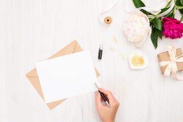 Obraz premium Top view woman hand writing wedding invitation card or love letter. Minimal flat lay composition with pion flowers, stationery stuff and feminine accessories. Writing letter concept.