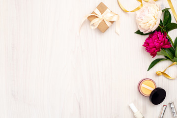 Top view frame made of women items : cosmetic, peony flowers, lipstick, gift box on wooden background. Minimal flat lay style composition with feminine accessories, home office desk concept.