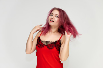 Fototapeta premium Concept portrait of a pretty sexy girl with purple hair in beautiful red lingerie on a white background. She smiles, happy with life, happy. Hair flying, front view. Made in a studio.