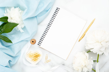 Obraz na płótnie Canvas Top view blank paper notepad, white peony flowers, blue scarf, golden clips on marble background. Minimal flat lay style composition with feminine accessories. Fashion or beauty blog banner mockup.