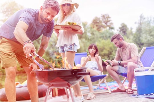 Man preparing food in barbecue grill with friends on pier