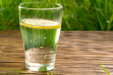 A glass of water with lemon on the background of fresh summer green grass