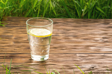 A glass of water with lemon on the background of fresh summer green grass