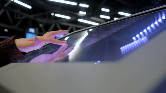 Woman using interactive touchscreen display of electronic multimedia kiosk at technology exhibition - scrolling and touching. Education, learning and technology concept