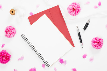 Home office desk workspace with blank paper notebook and pink rose flower buds and petals on white background. Minimal flat lay style composition. Top view feminine background.