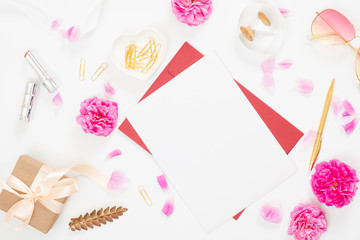 Flat lay home office desk. Top view blank paper card, pink rose flower buds, petals, female accessories, gift box on white background. Women desk, fashion blogger, beauty concept.