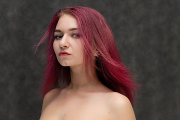 Concept portrait of a close-up of a pretty sexy girl with purple hair on a gray background. She...