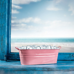 Blue retro old window sill with free space for your product. Cold wet ice in metal container. Landscape of beach with blue sky. 
